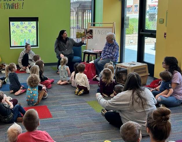 Librarian reading a book to children who are seated on the floor.